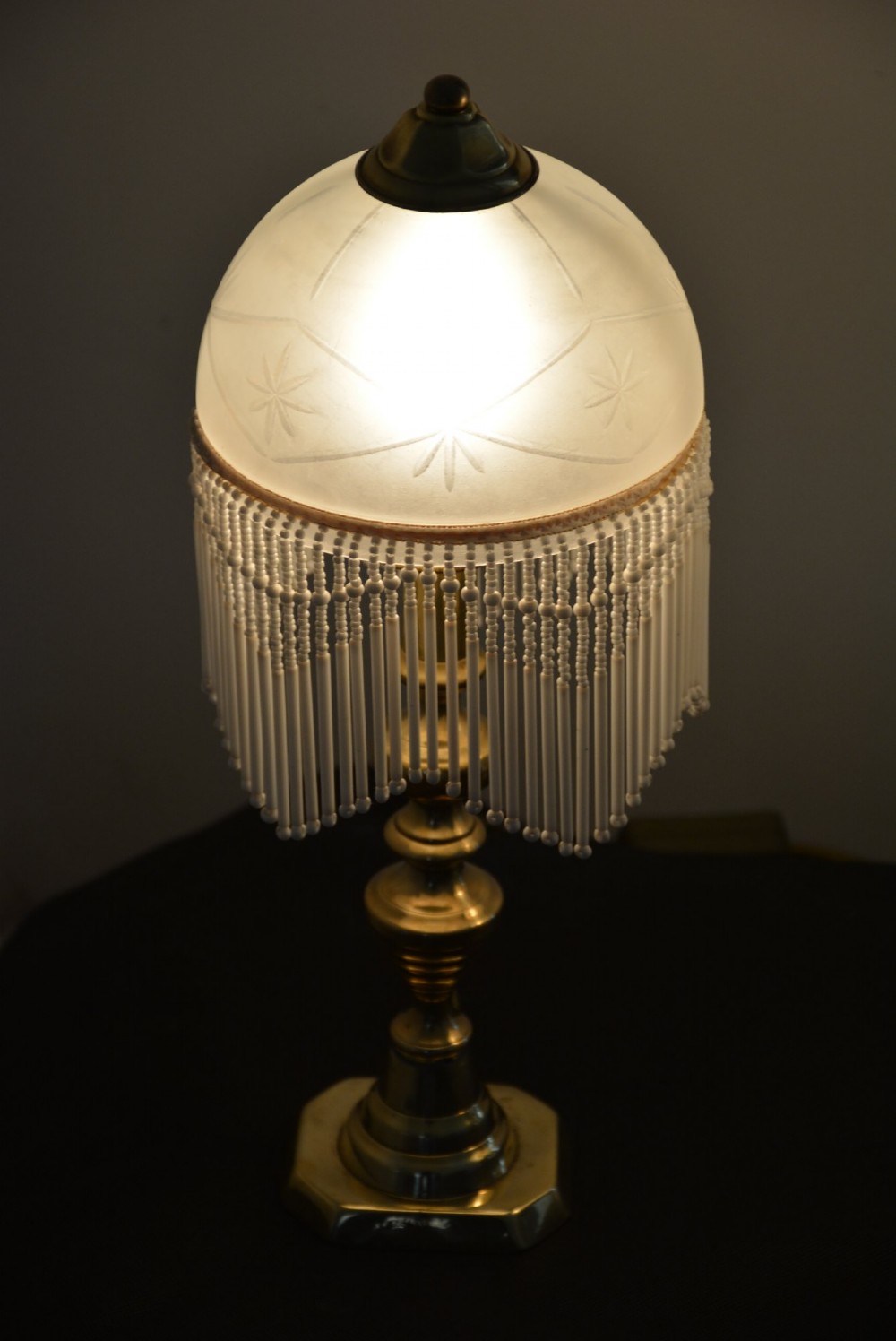 A pair of illuminated Victorian turned brass table lamps featuring etched frosted glass dome shades with beaded fringe hanging around the rim. View IV