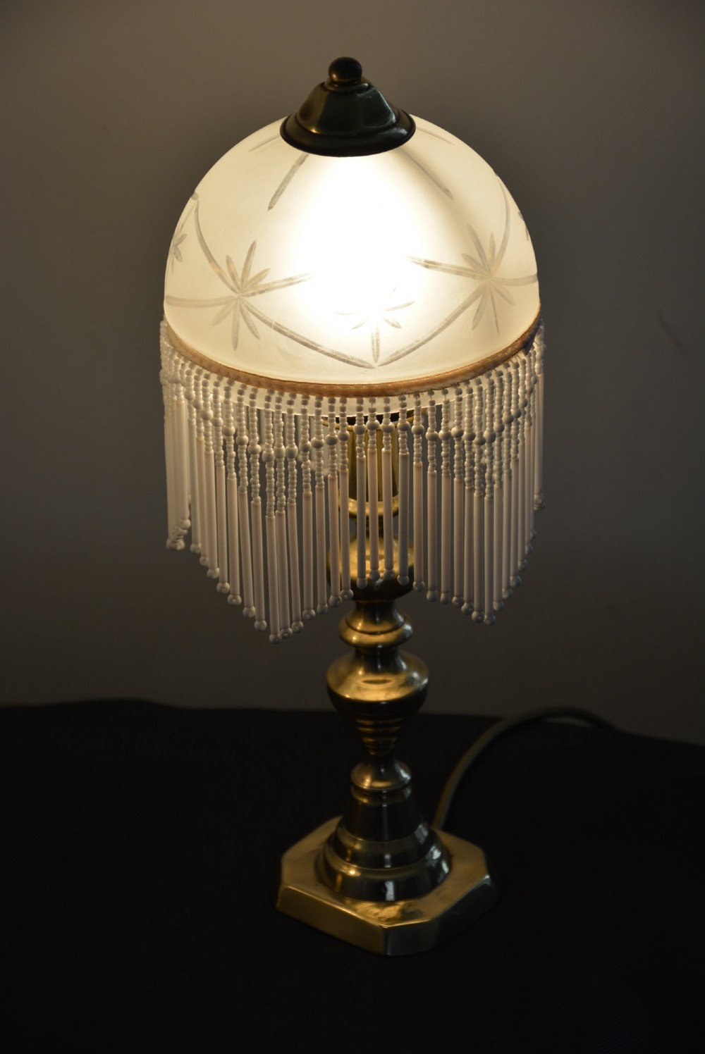 A pair of illuminated Victorian turned brass table lamps featuring etched frosted glass dome shades with beaded fringe hanging around the rim. View V