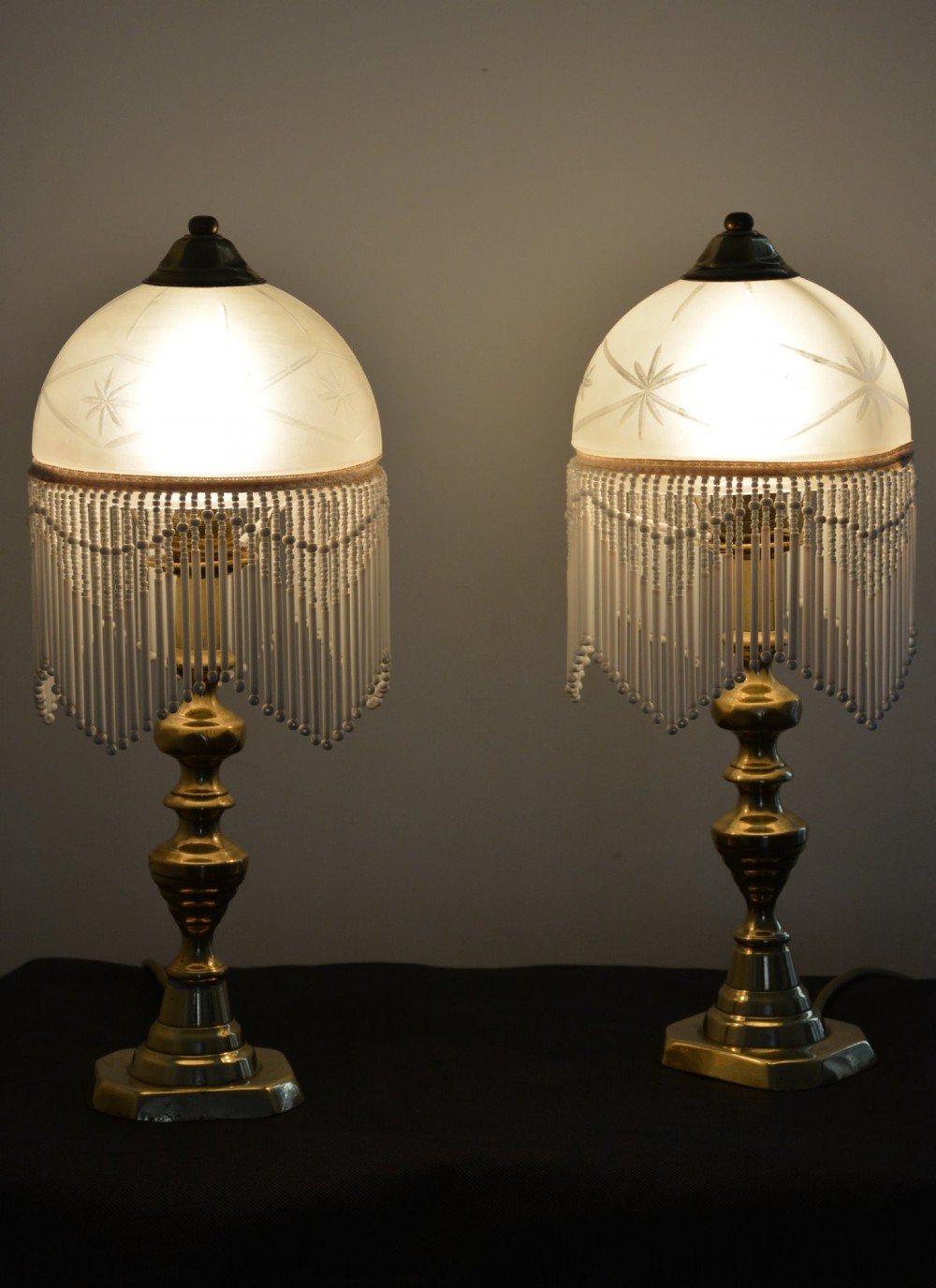 A pair of illuminated Victorian turned brass table lamps featuring etched frosted glass dome shades with beaded fringe hanging around the rim. View VI