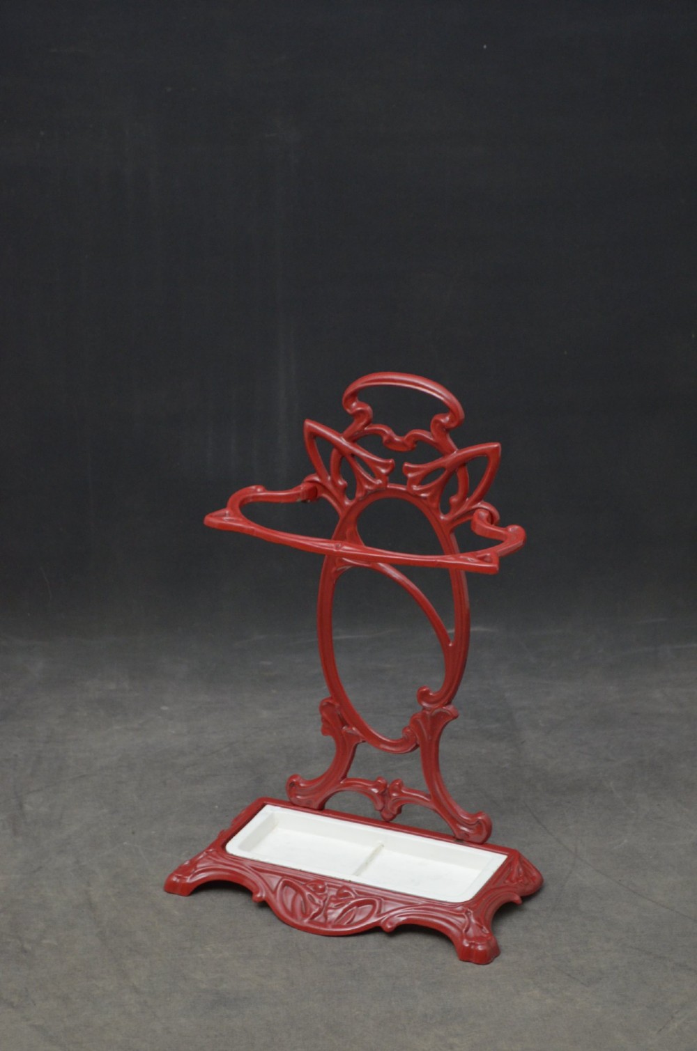 A red painted cast iron Art Nouveau umbrella stand with stylized openwork back plate and white divided base tray. View II