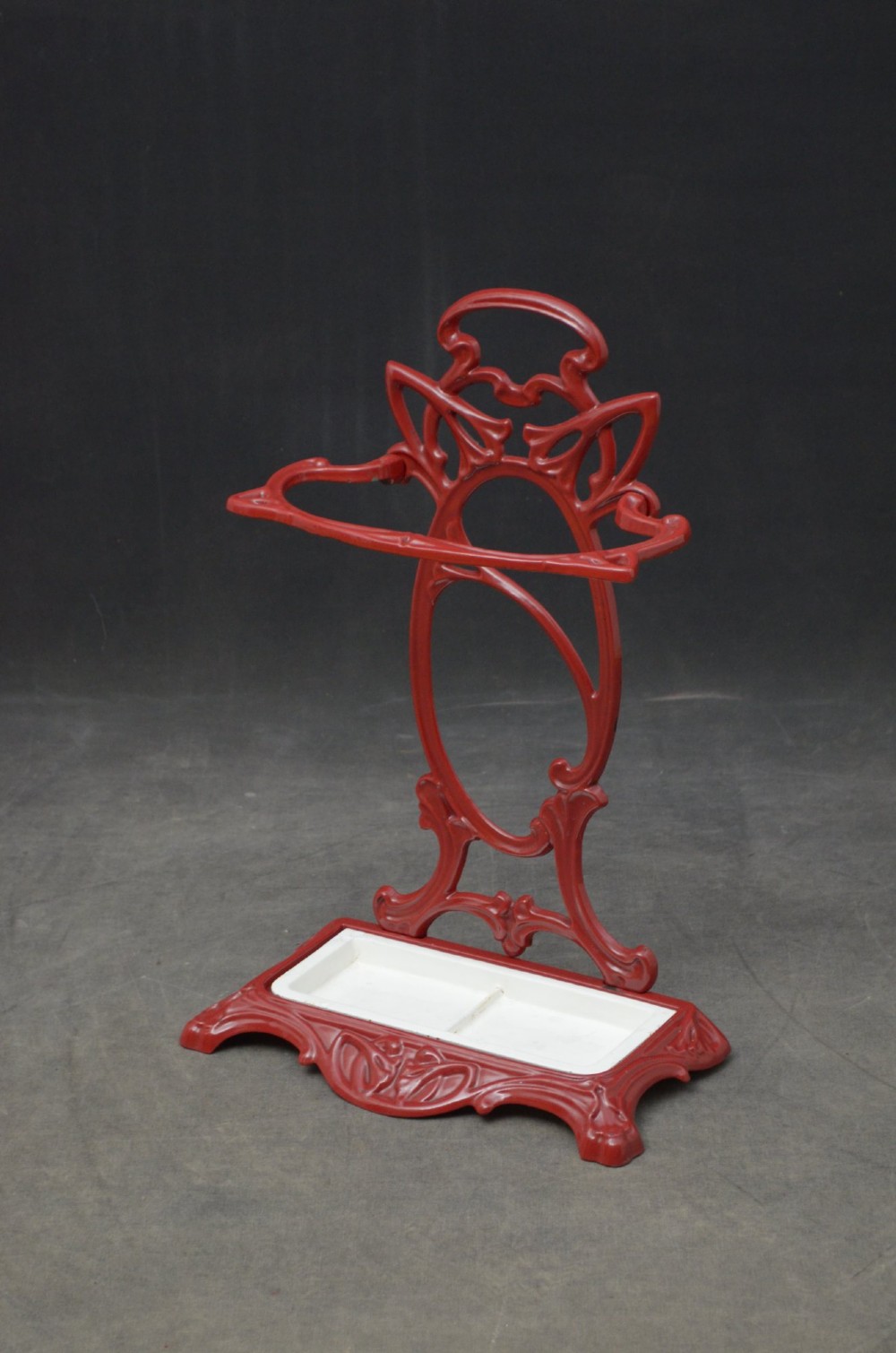 A red painted cast iron Art Nouveau umbrella stand with stylized openwork back plate and white divided base tray.