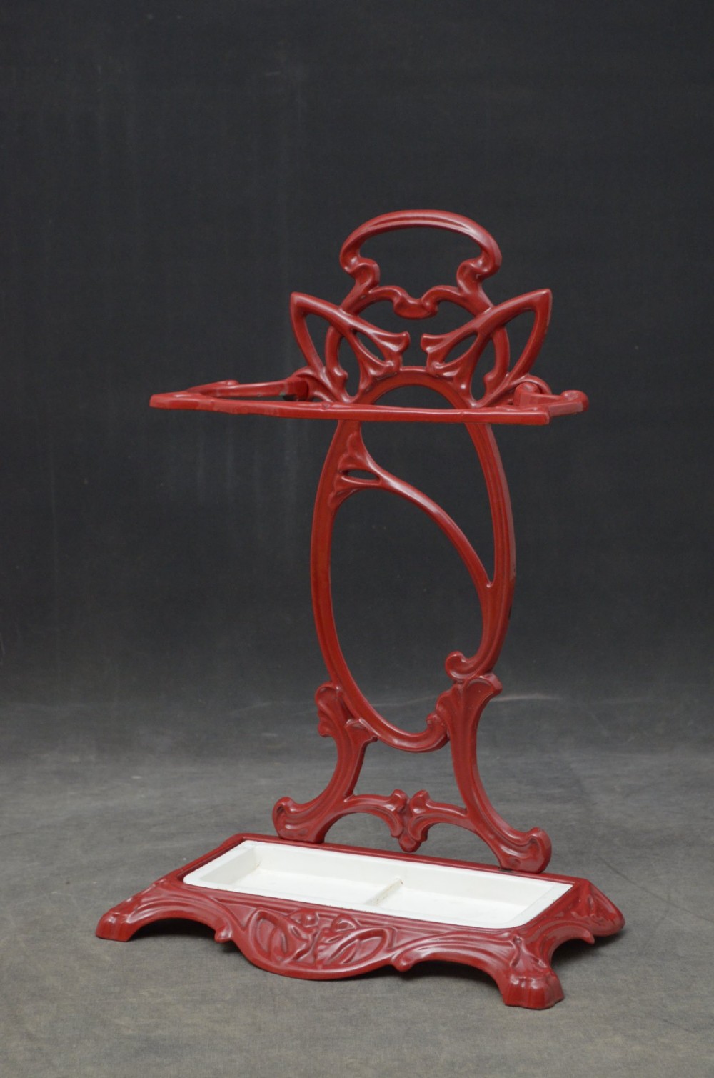 A red painted cast iron Art Nouveau umbrella stand with stylized openwork back plate and white divided base tray. View III