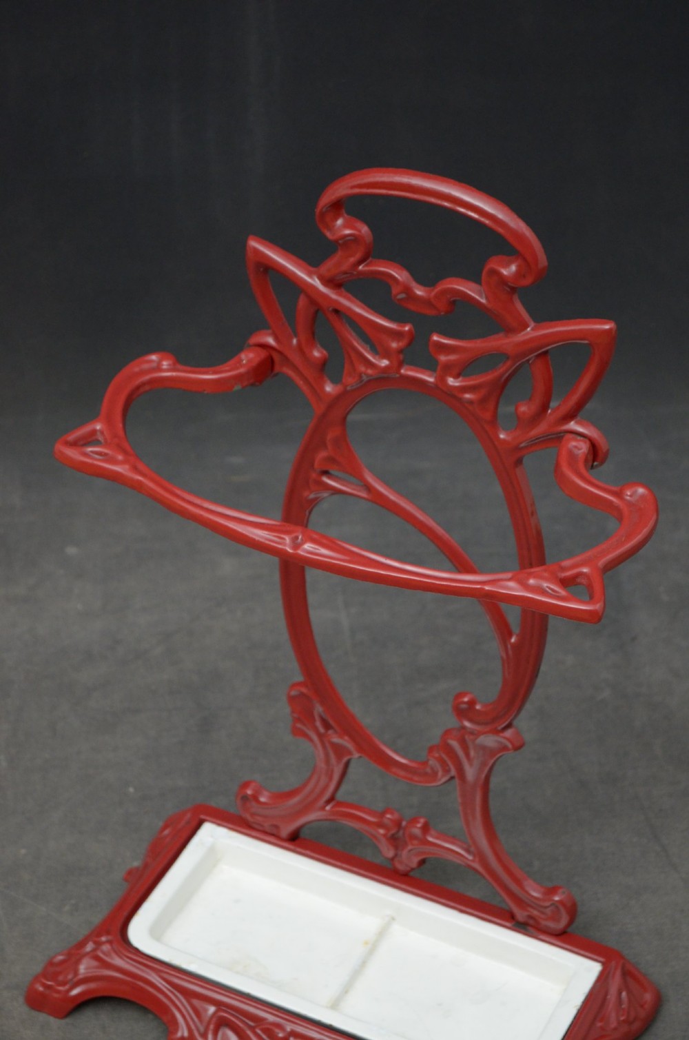 A red painted cast iron Art Nouveau umbrella stand with stylized openwork back plate and white divided base tray. View IV