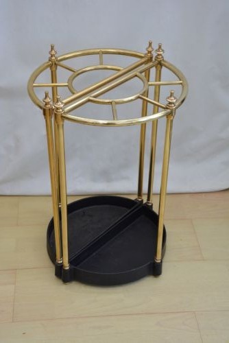 A pair of early 20th-century semi-circular brass umbrella stands with finial posts and black cast iron drip trays, placed back to back. View II