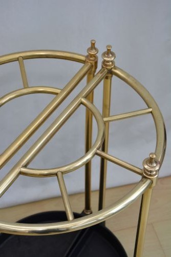 A pair of early 20th-century semi-circular brass umbrella stands with finial posts and black cast iron drip trays, placed back to back. View V