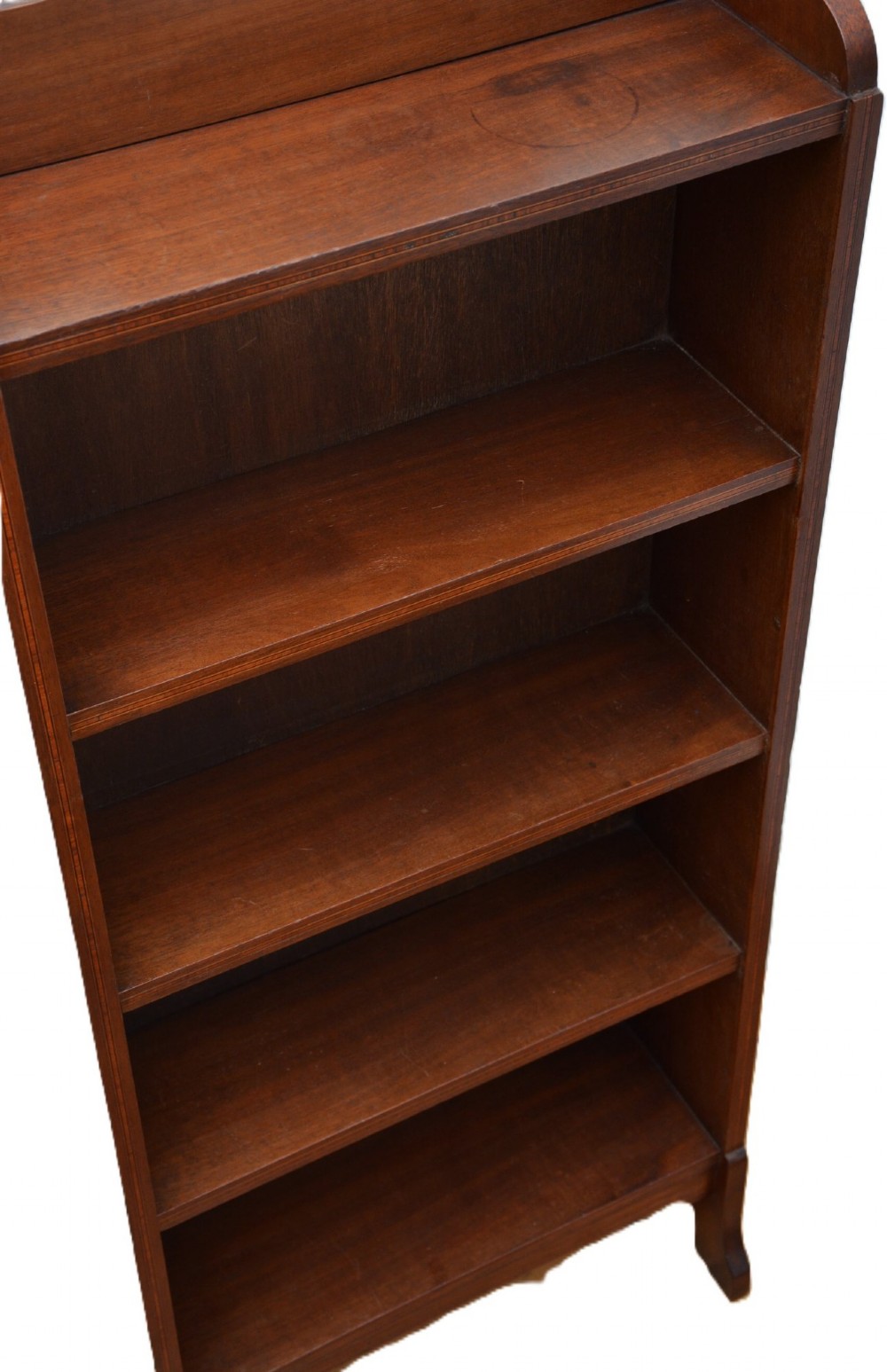 A slim Edwardian mahogany open bookcase featuring four shelves, an inlaid oval motif on the shaped gallery top, and bracket feet. View IV