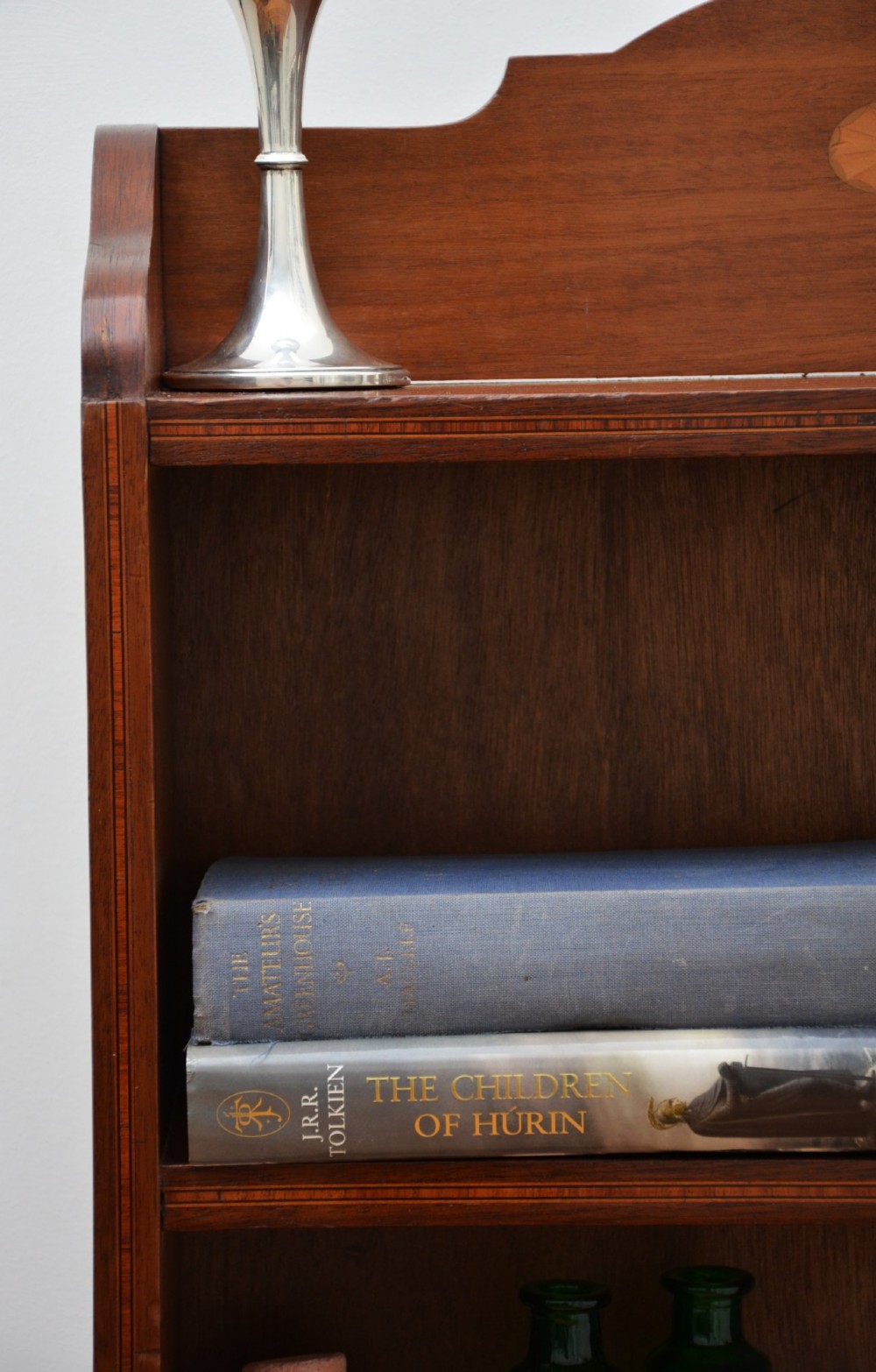 A slim Edwardian mahogany open bookcase featuring four shelves, an inlaid oval motif on the shaped gallery top, and bracket feet. View V