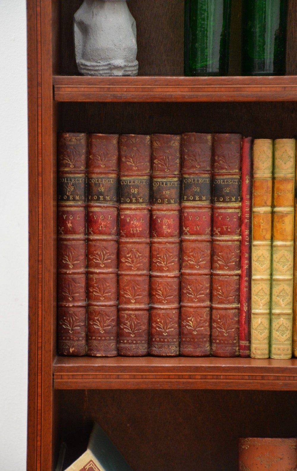 A slim Edwardian mahogany open bookcase featuring four shelves, an inlaid oval motif on the shaped gallery top, and bracket feet. View VI