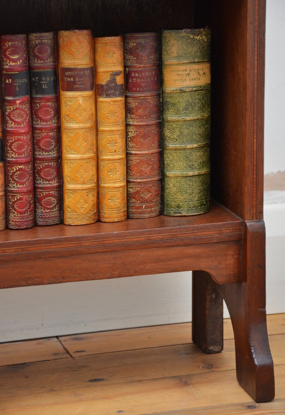 A slim Edwardian mahogany open bookcase featuring four shelves, an inlaid oval motif on the shaped gallery top, and bracket feet. View VII