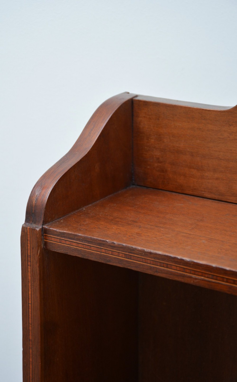 A slim Edwardian mahogany open bookcase featuring four shelves, an inlaid oval motif on the shaped gallery top, and bracket feet. View XIV