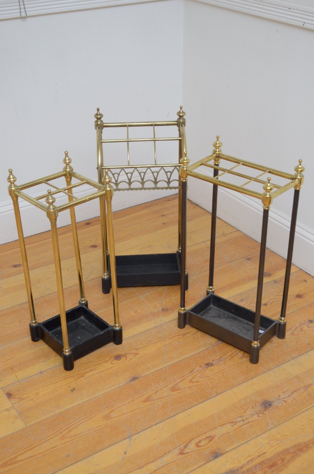 A Victorian tubular brass umbrella stand featuring a curved upper section with internal divisions, finial caps, a arched fretwork apron, and a black cast iron drip tray base. View II
