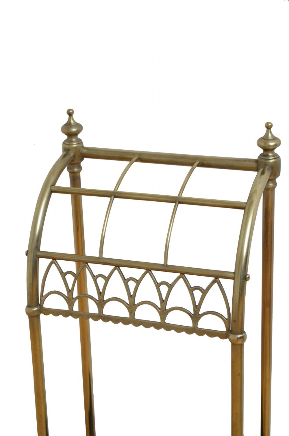 A Victorian tubular brass umbrella stand featuring a curved upper section with internal divisions, finial caps, a arched fretwork apron, and a black cast iron drip tray base. View IV