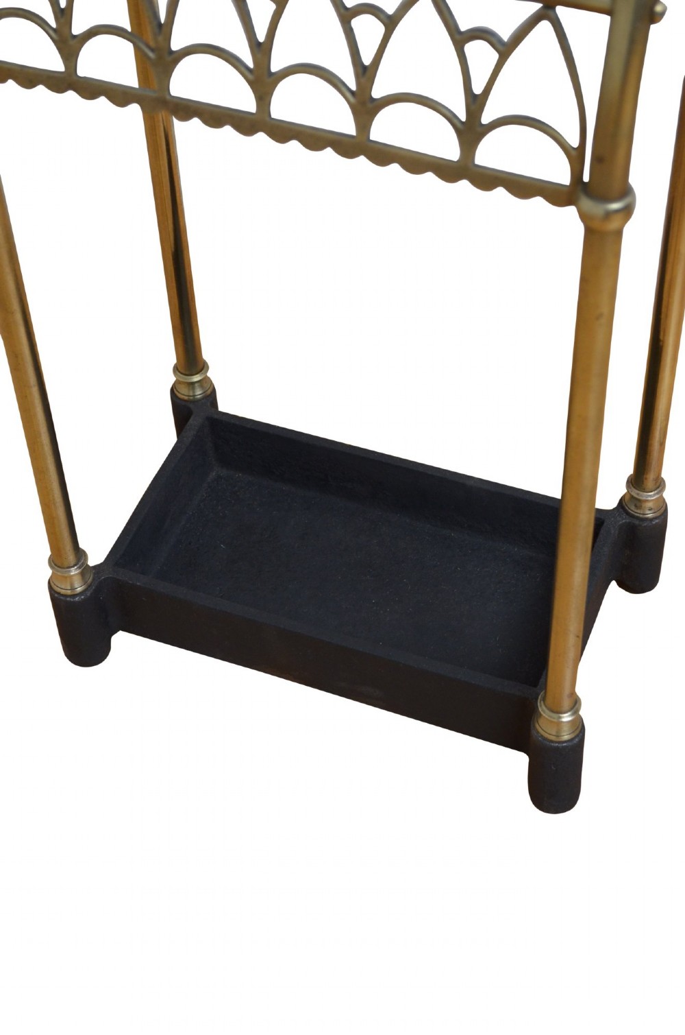 A Victorian tubular brass umbrella stand featuring a curved upper section with internal divisions, finial caps, a arched fretwork apron, and a black cast iron drip tray base. View VII