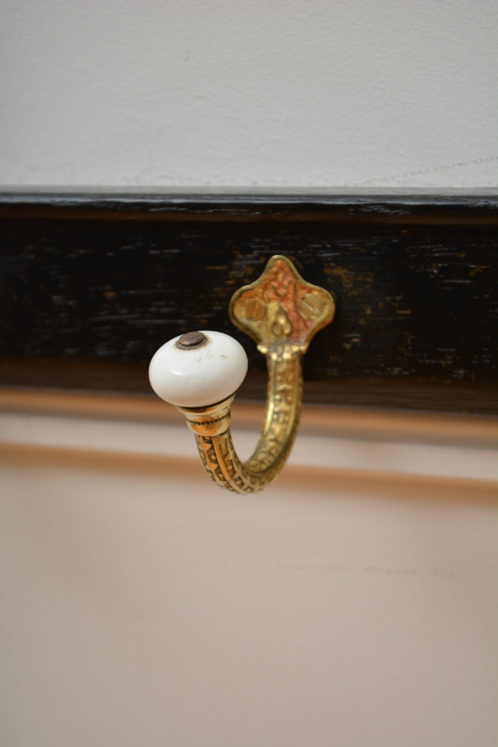 An ebonised black wooden wall rack featuring four cast brass hooks with white ceramic terminal knobs. View II