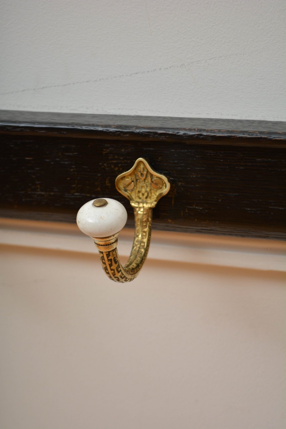 An ebonised black wooden wall rack featuring four cast brass hooks with white ceramic terminal knobs. View III