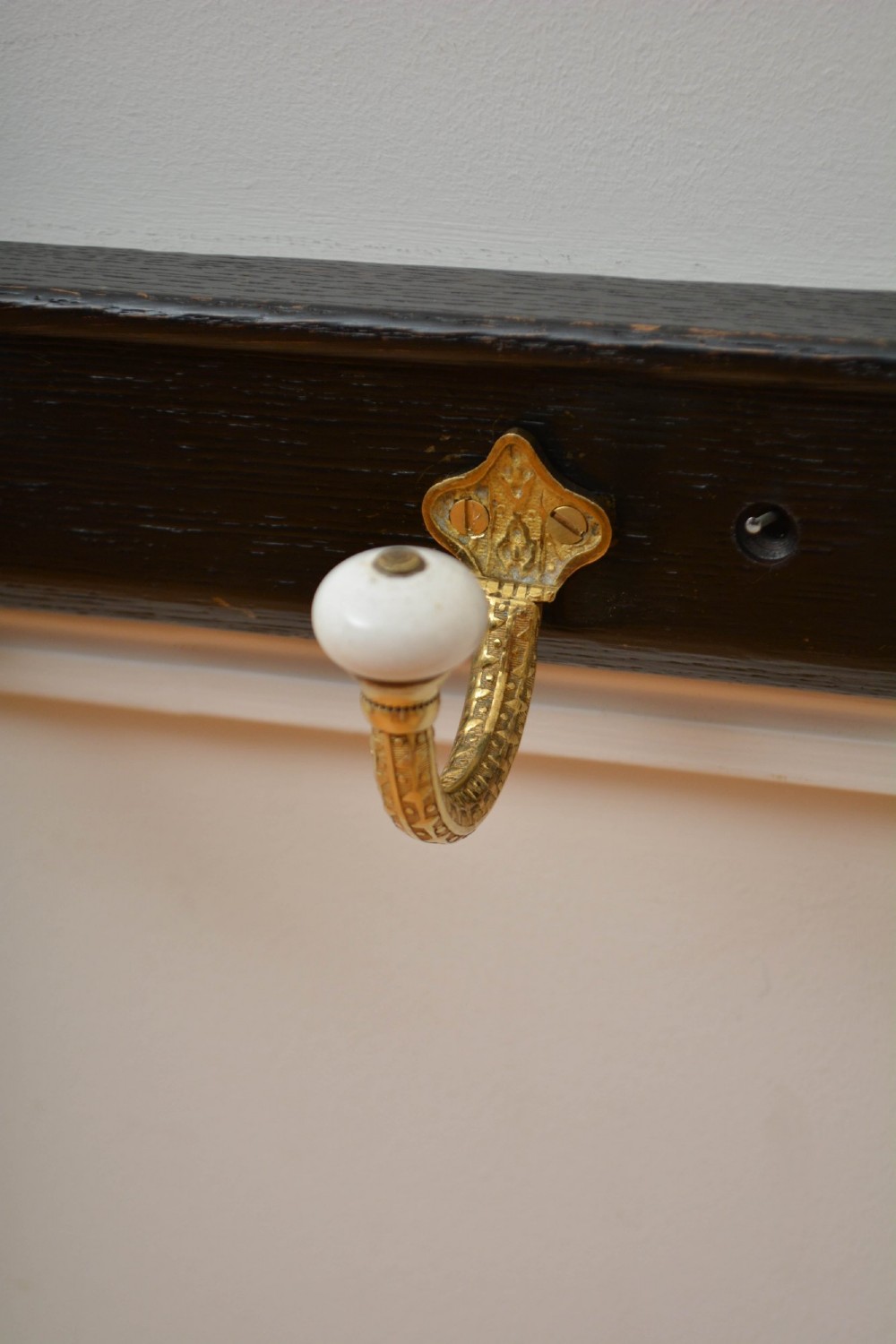 An ebonised black wooden wall rack featuring four cast brass hooks with white ceramic terminal knobs. View IV