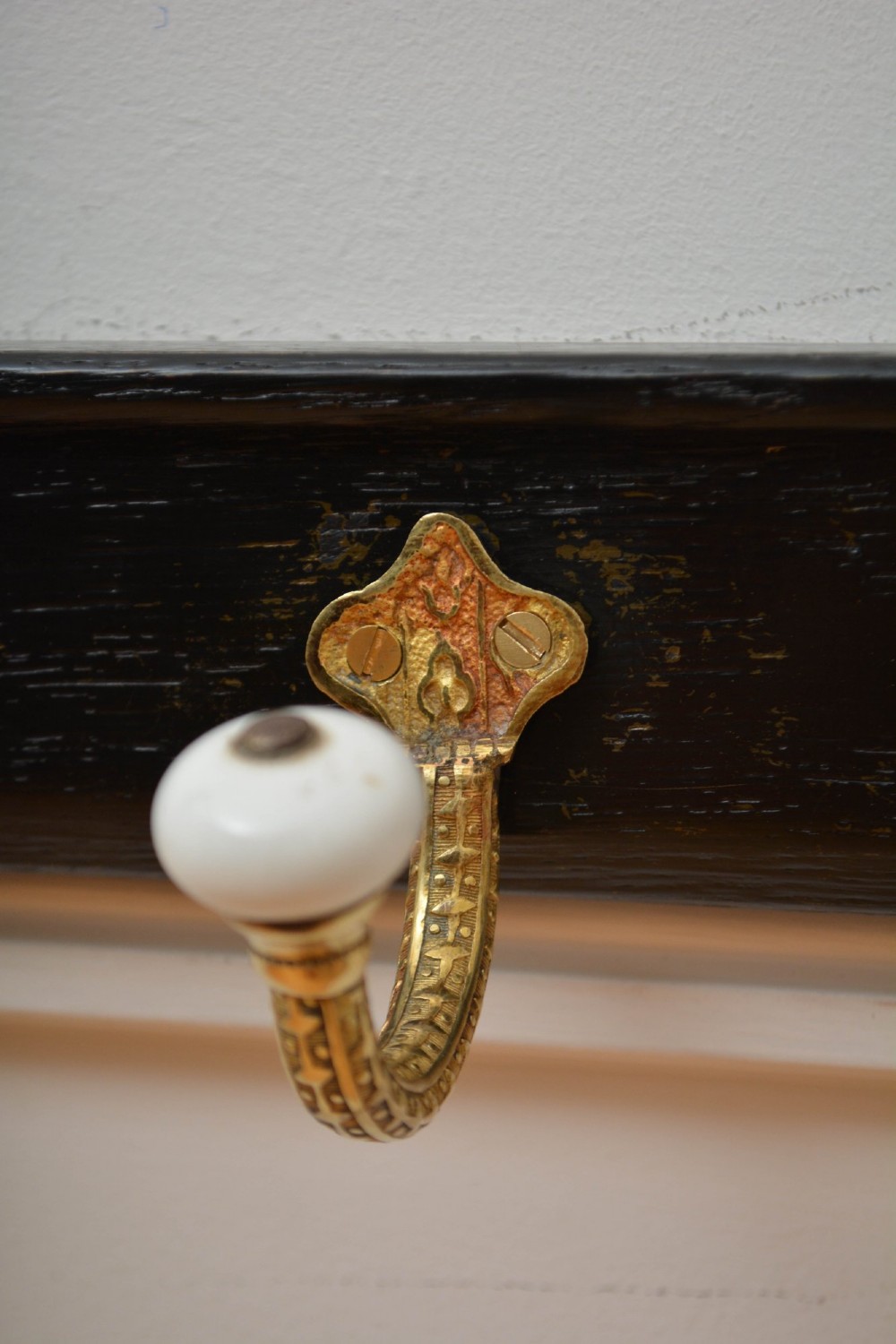 An ebonised black wooden wall rack featuring four cast brass hooks with white ceramic terminal knobs. View V