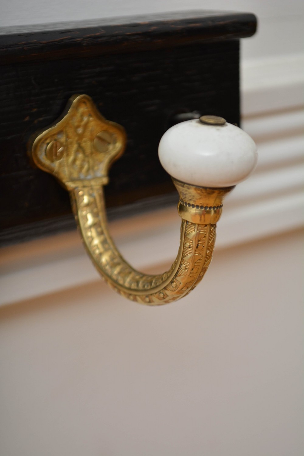 An ebonised black wooden wall rack featuring four cast brass hooks with white ceramic terminal knobs. View VI