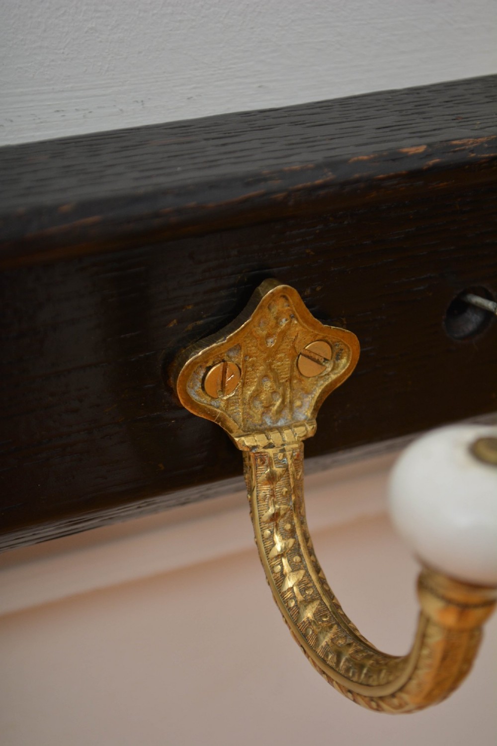 An ebonised black wooden wall rack featuring four cast brass hooks with white ceramic terminal knobs. View VII