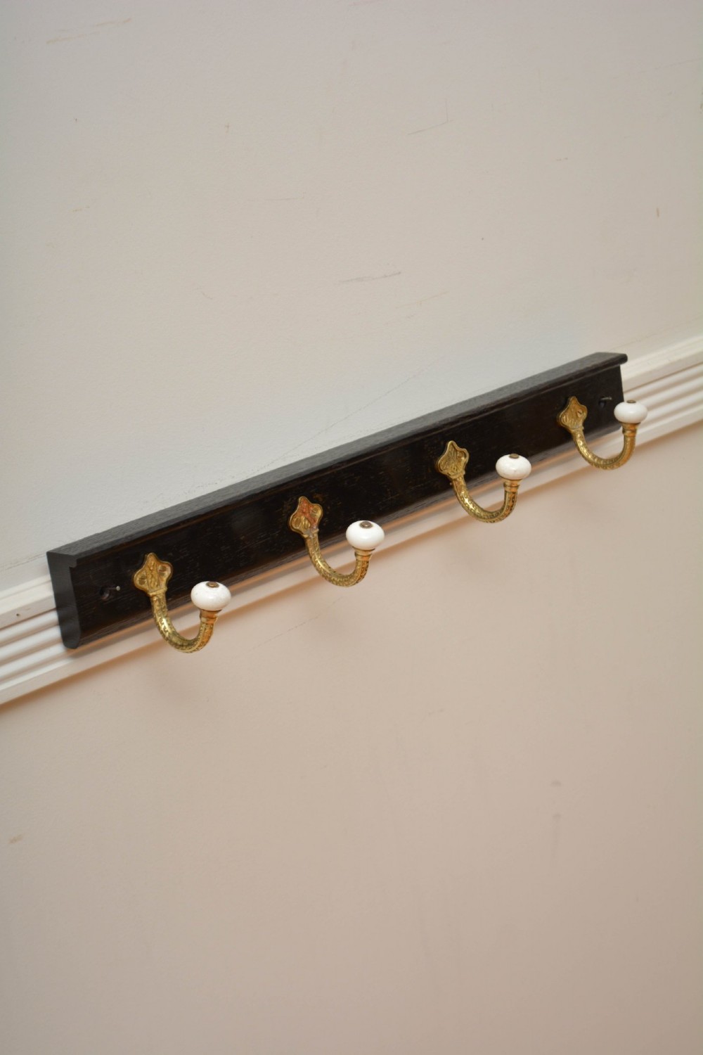 An ebonised black wooden wall rack featuring four cast brass hooks with white ceramic terminal knobs. View IX