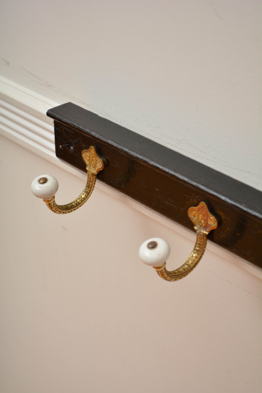 An ebonised black wooden wall rack featuring four cast brass hooks with white ceramic terminal knobs. View XII