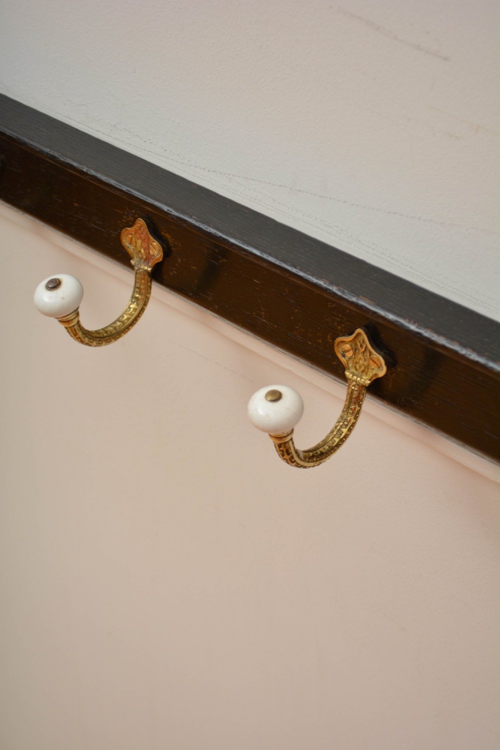 An ebonised black wooden wall rack featuring four cast brass hooks with white ceramic terminal knobs. View XIII