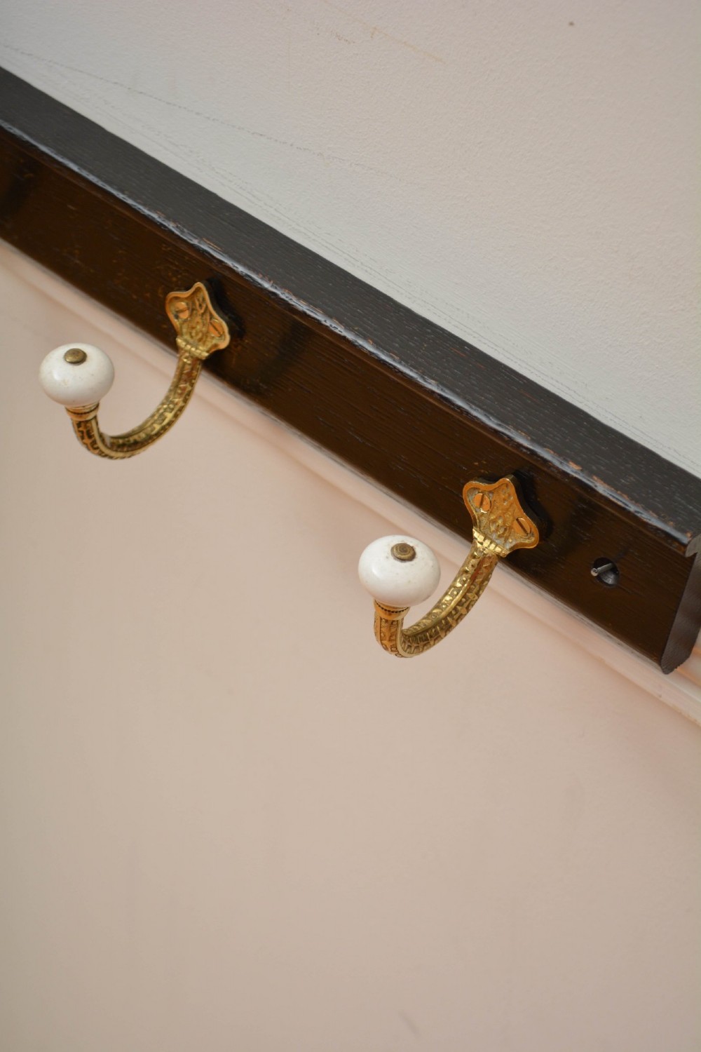 An ebonised black wooden wall rack featuring four cast brass hooks with white ceramic terminal knobs. View XIV