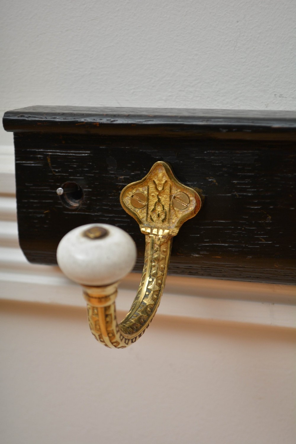 An ebonised black wooden wall rack featuring four cast brass hooks with white ceramic terminal knobs. View XV