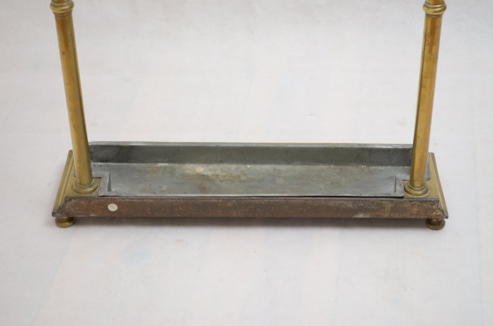 A Victorian brass umbrella stand featuring three divided upper slots, vertical supports, small bun feet, and a metal drip tray. View II
