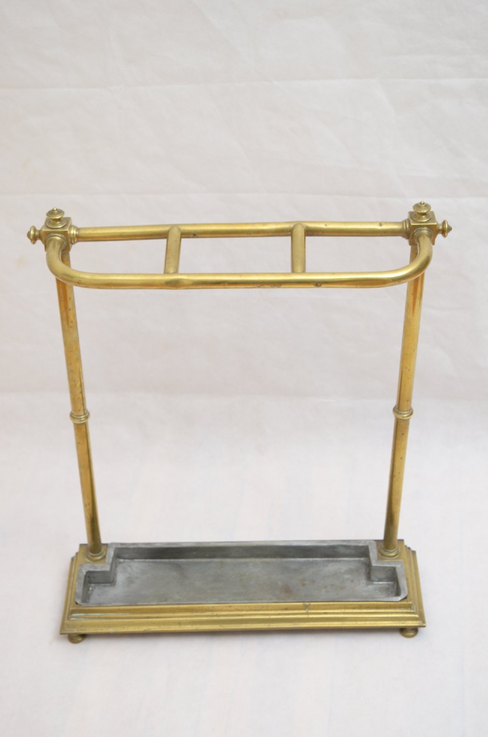 A Victorian brass umbrella stand featuring three divided upper slots, vertical supports, small bun feet, and a metal drip tray. View III