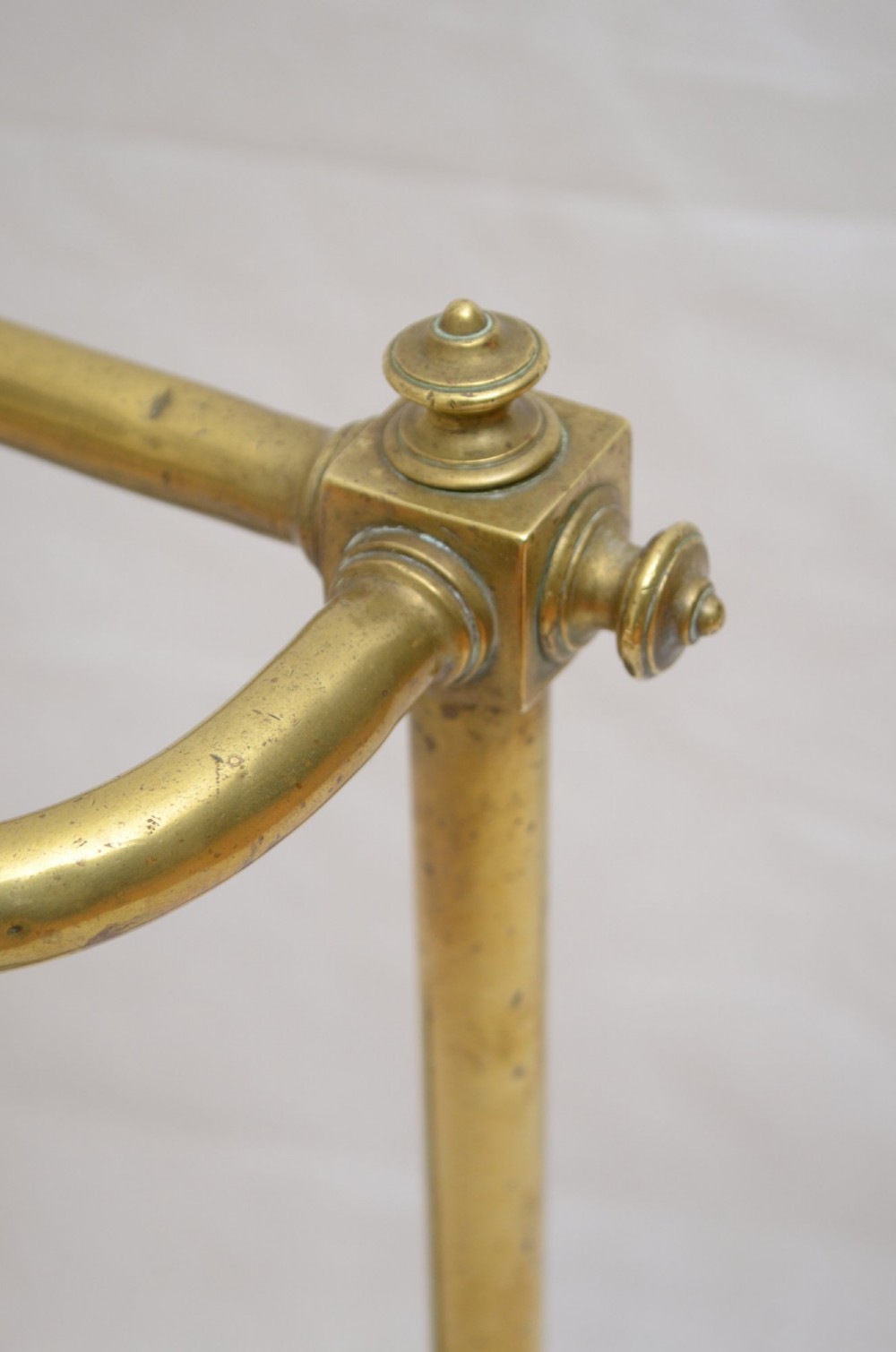A Victorian brass umbrella stand featuring three divided upper slots, vertical supports, small bun feet, and a metal drip tray. View V