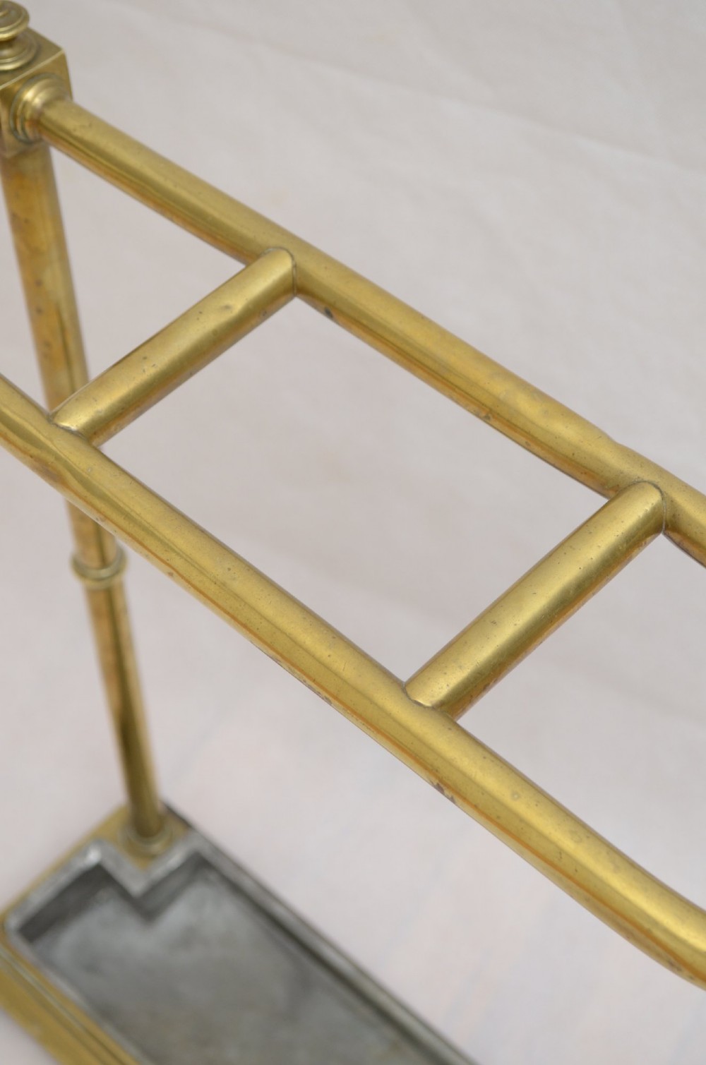 A Victorian brass umbrella stand featuring three divided upper slots, vertical supports, small bun feet, and a metal drip tray. View VI
