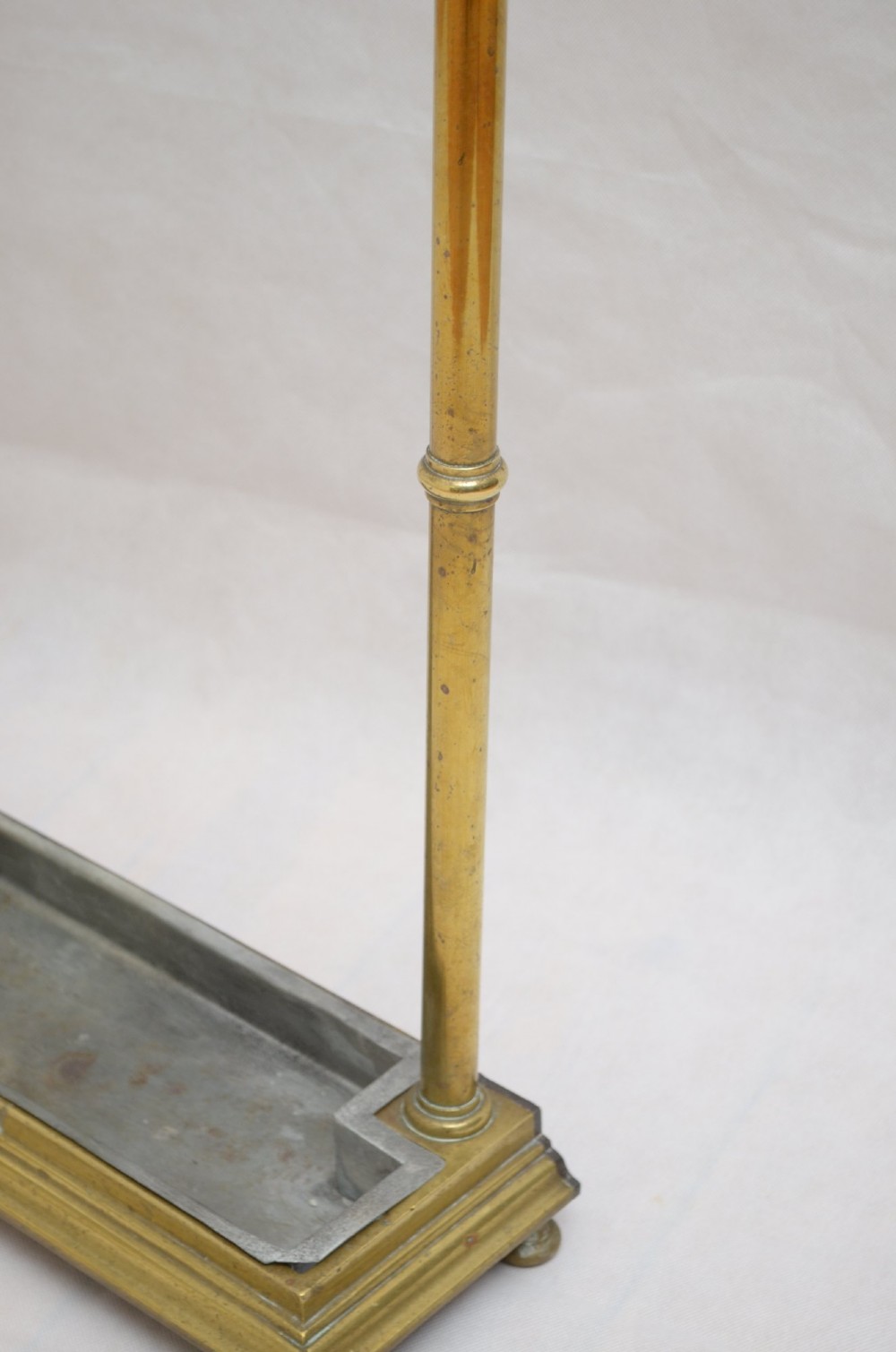 A Victorian brass umbrella stand featuring three divided upper slots, vertical supports, small bun feet, and a metal drip tray. View VII