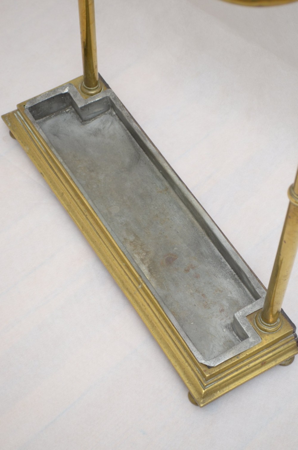 A Victorian brass umbrella stand featuring three divided upper slots, vertical supports, small bun feet, and a metal drip tray. View VIII