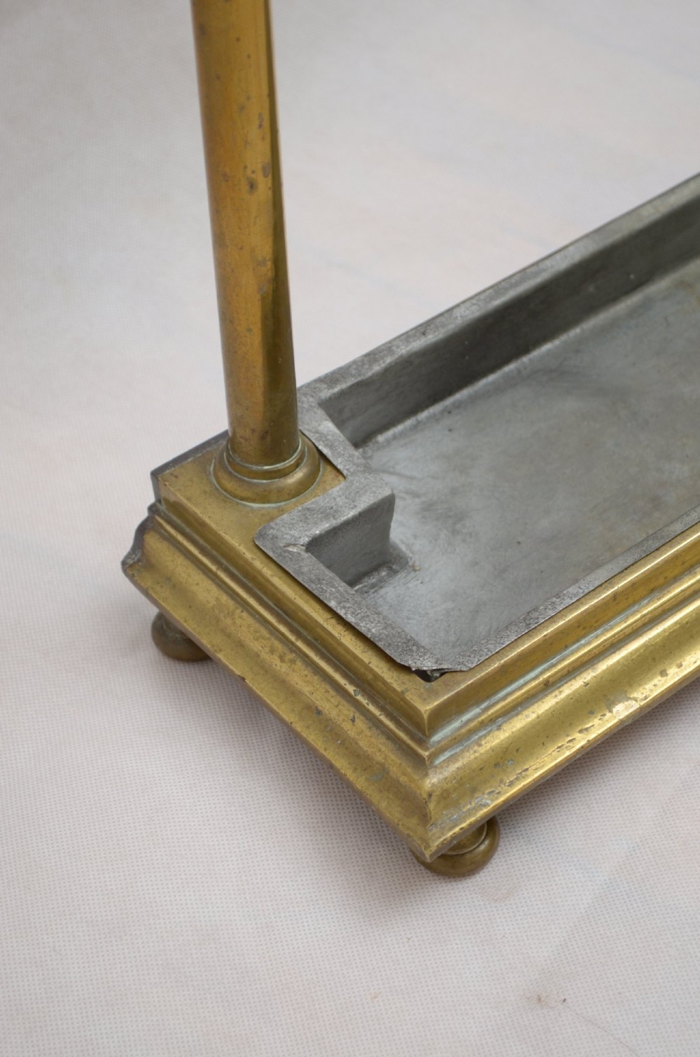 A Victorian brass umbrella stand featuring three divided upper slots, vertical supports, small bun feet, and a metal drip tray. View IX