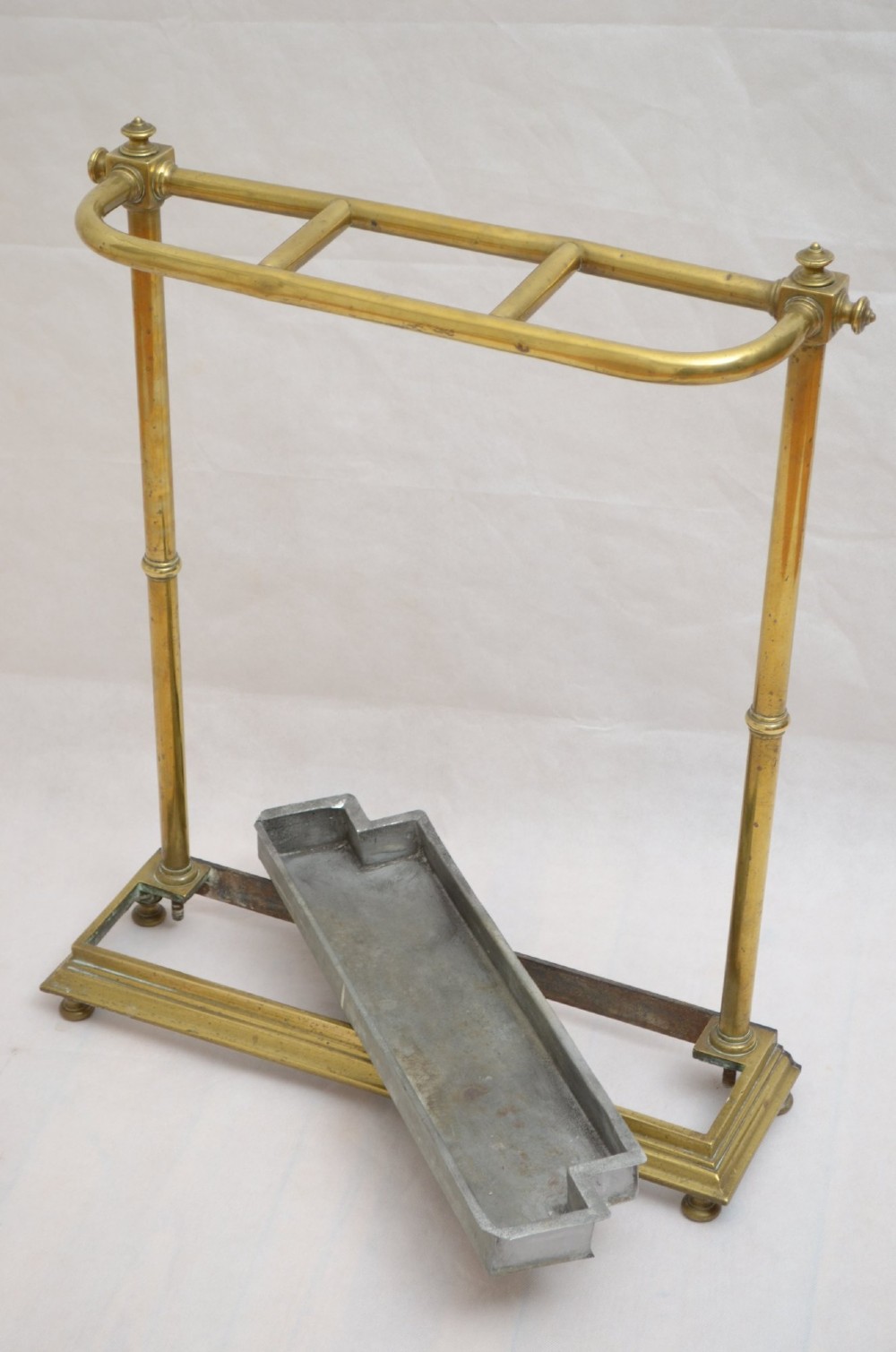 A Victorian brass umbrella stand featuring three divided upper slots, vertical supports, small bun feet, and a metal drip tray. View X