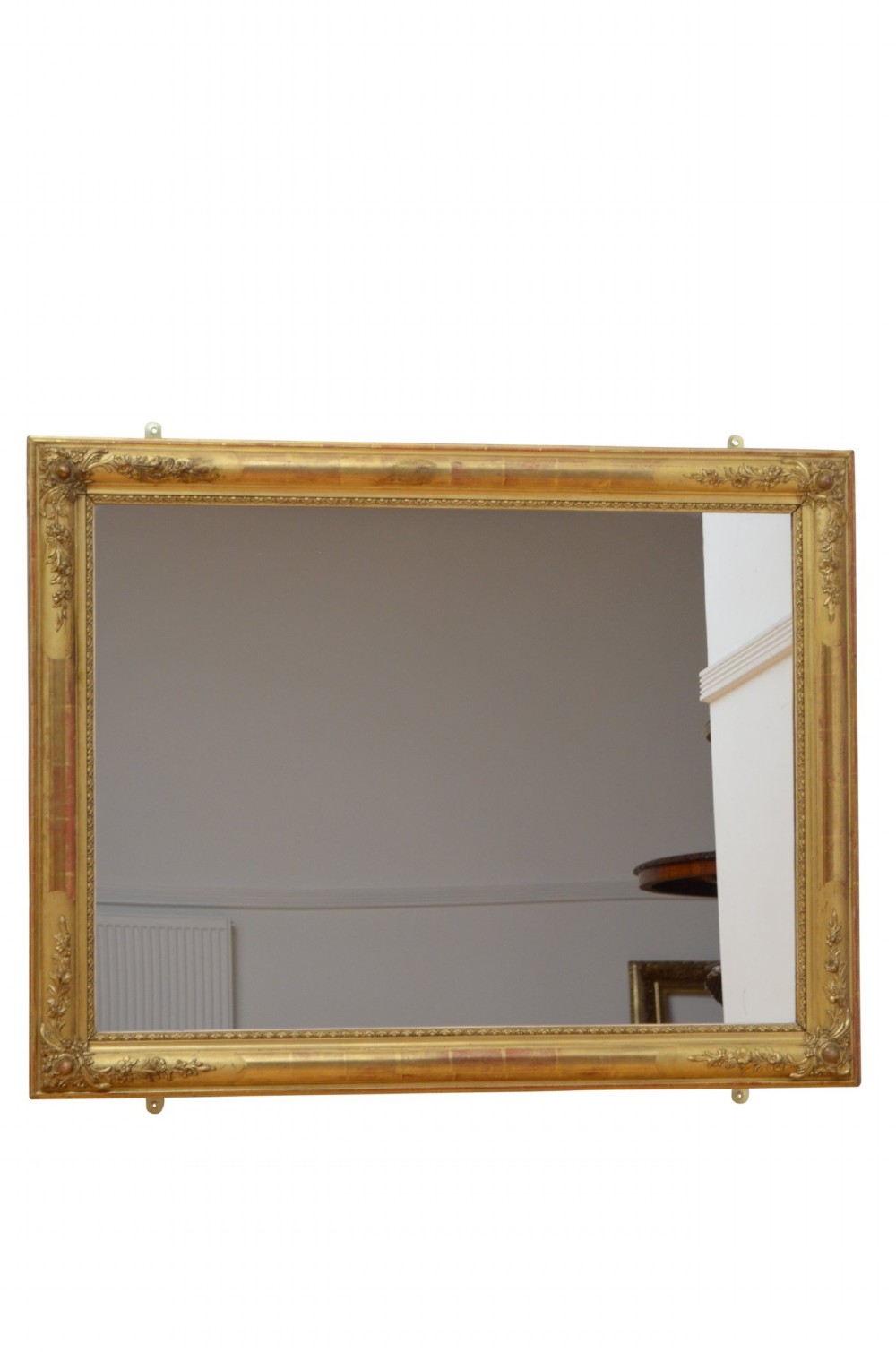 A large rectangular antique giltwood wall mirror with carved floral corner details and a beaded inner border.