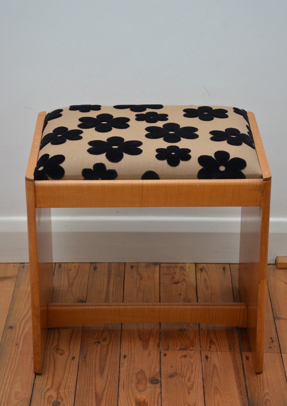 An Art Deco sycamore wood dressing stool featuring slab side legs, a low cylindrical stretcher, and a padded seat upholstered in beige fabric with black floral motifs. View III
