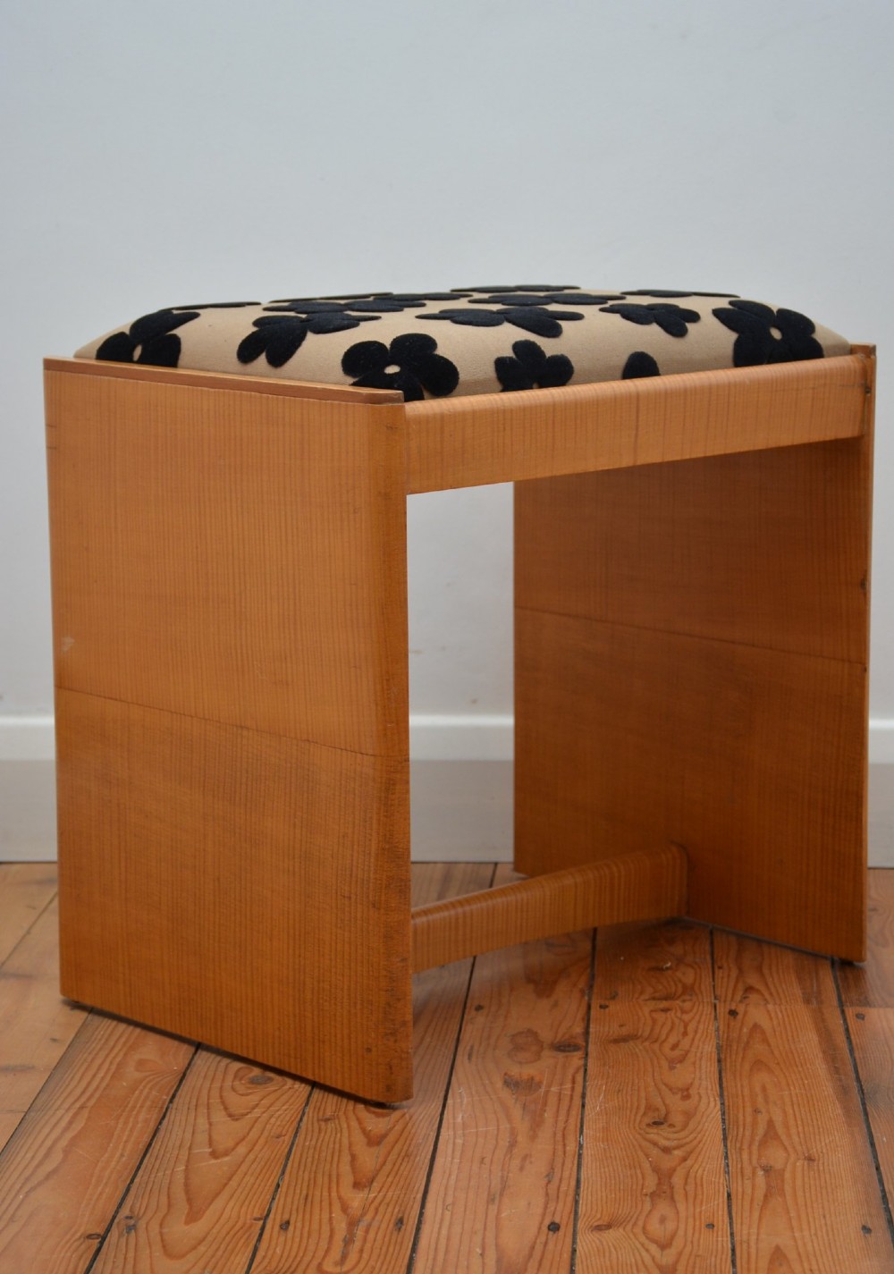 An Art Deco sycamore wood dressing stool featuring slab side legs, a low cylindrical stretcher, and a padded seat upholstered in beige fabric with black floral motifs. View IV