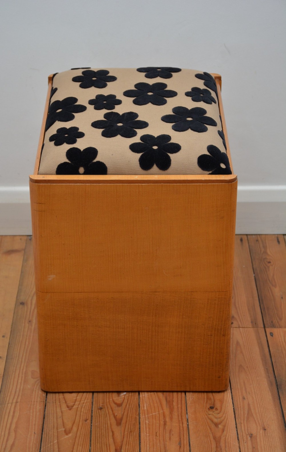 An Art Deco sycamore wood dressing stool featuring slab side legs, a low cylindrical stretcher, and a padded seat upholstered in beige fabric with black floral motifs. View V
