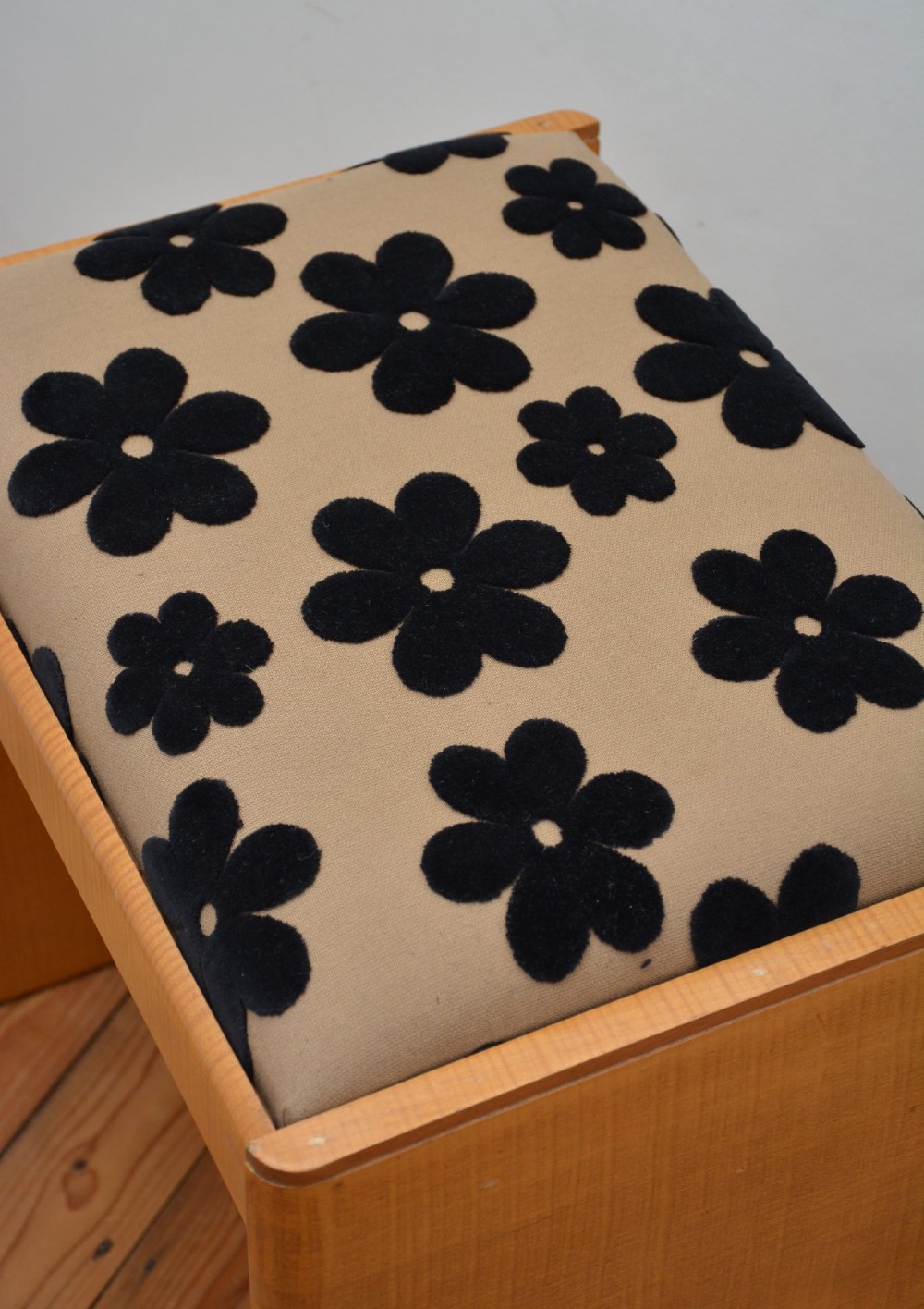 An Art Deco sycamore wood dressing stool featuring slab side legs, a low cylindrical stretcher, and a padded seat upholstered in beige fabric with black floral motifs. View VI