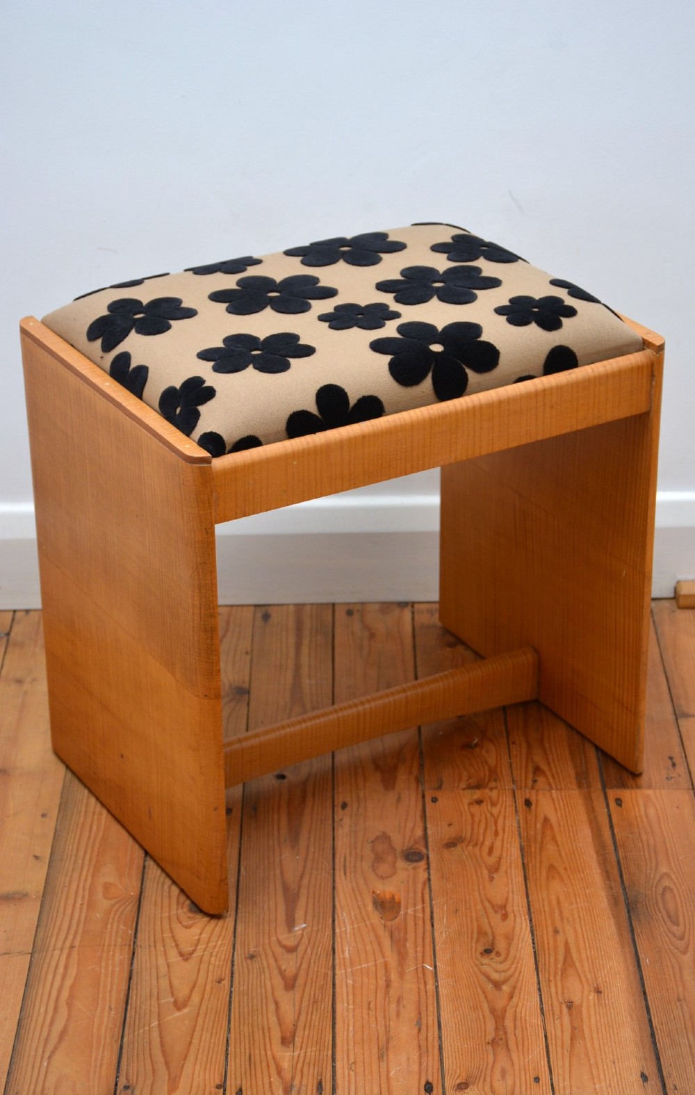 An Art Deco sycamore wood dressing stool featuring slab side legs, a low cylindrical stretcher, and a padded seat upholstered in beige fabric with black floral motifs. View IX