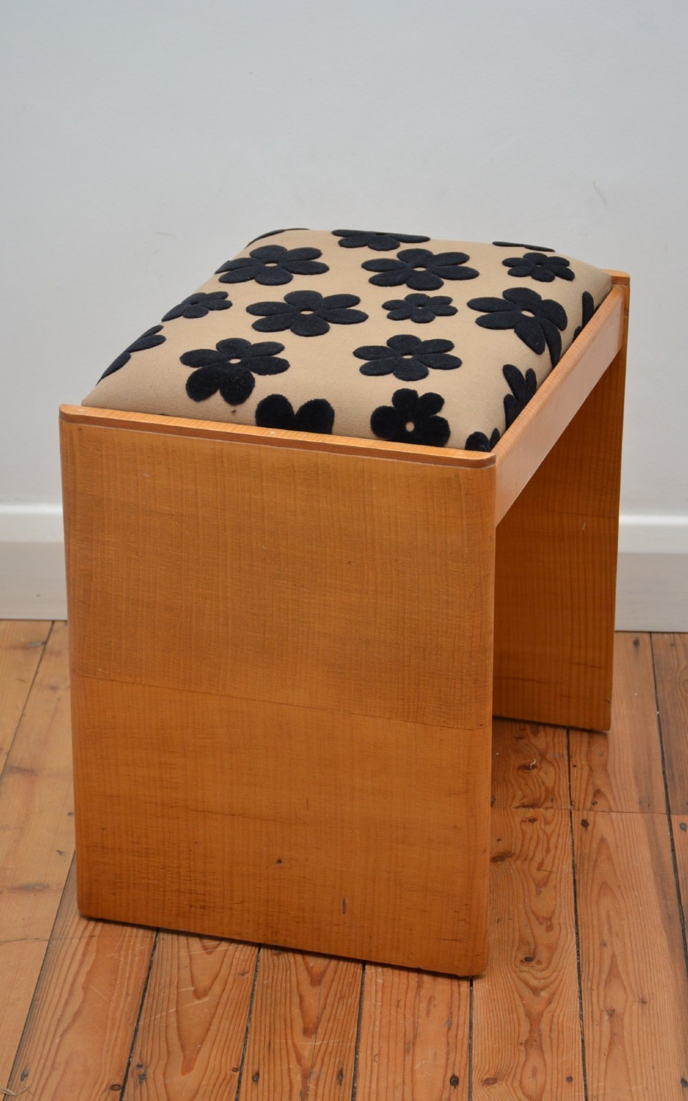 An Art Deco sycamore wood dressing stool featuring slab side legs, a low cylindrical stretcher, and a padded seat upholstered in beige fabric with black floral motifs. View XI