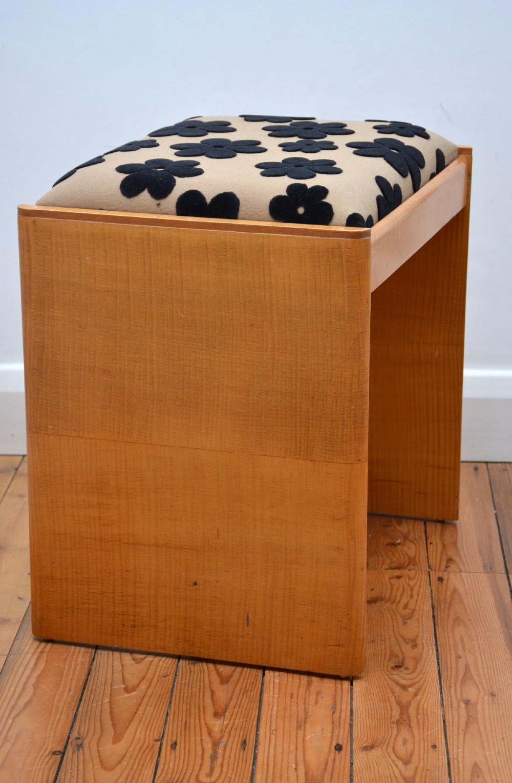 An Art Deco sycamore wood dressing stool featuring slab side legs, a low cylindrical stretcher, and a padded seat upholstered in beige fabric with black floral motifs. View XII