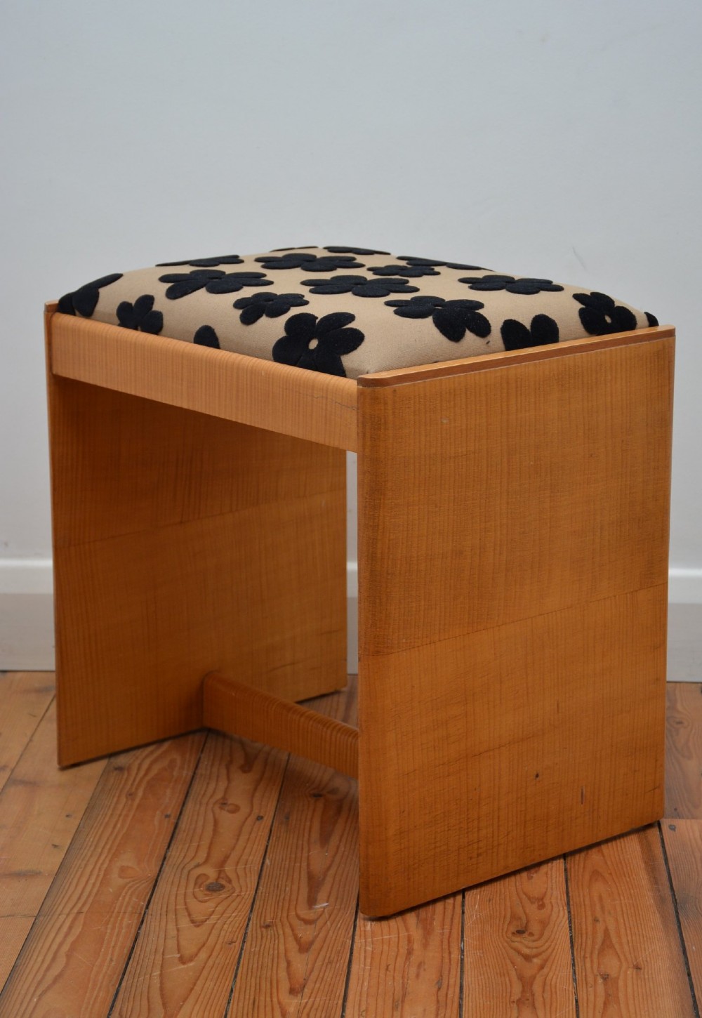 An Art Deco sycamore wood dressing stool featuring slab side legs, a low cylindrical stretcher, and a padded seat upholstered in beige fabric with black floral motifs. View XIII