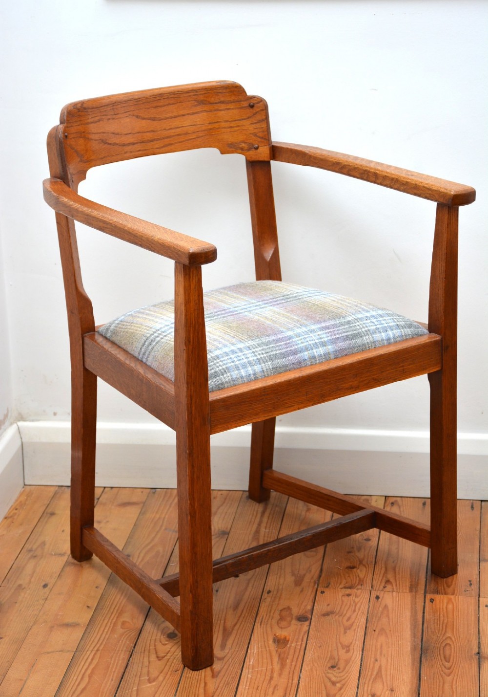 An oak Arts and Crafts desk chair featuring straight armrests, a rectangular backrest, and a blue and grey plaid upholstered seat.