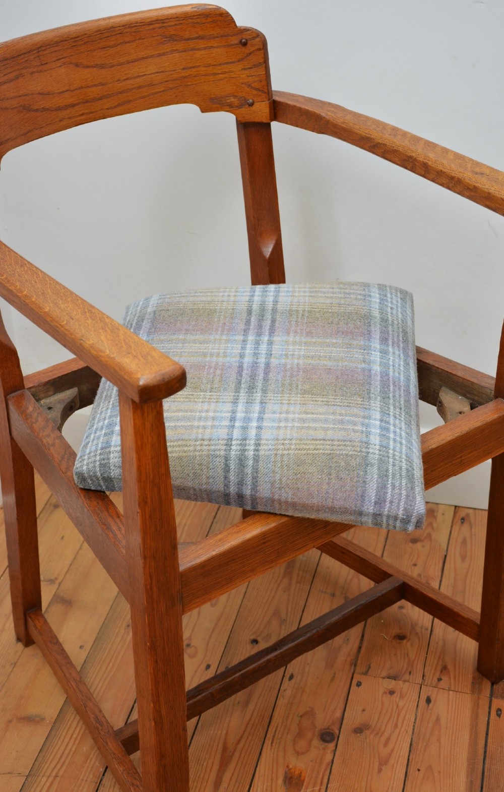 An oak Arts and Crafts desk chair featuring straight armrests, a rectangular backrest, and a blue and grey plaid upholstered seat. View X