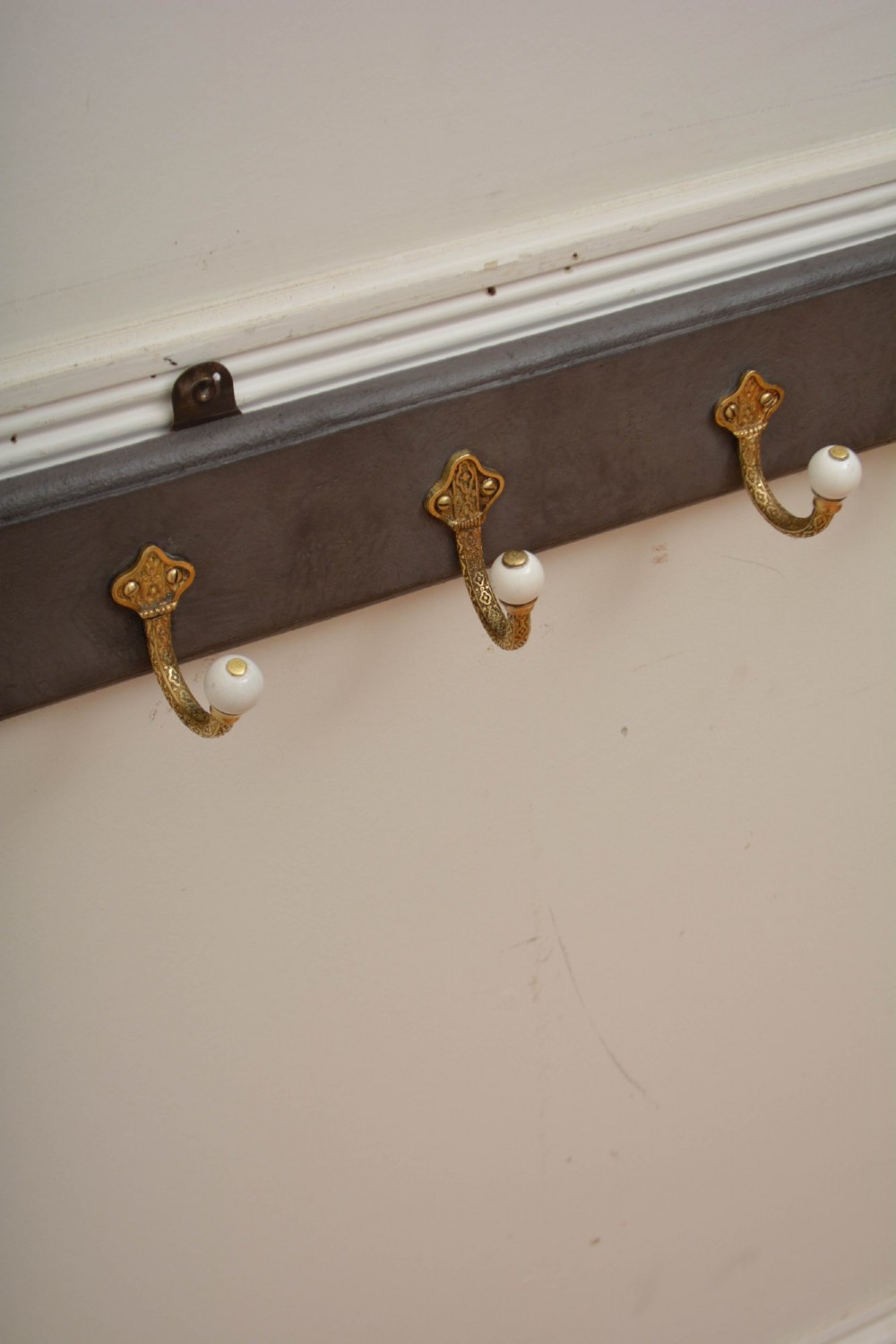A long dark timber wall-mounted coat rack featuring multiple cast brass hooks with white ceramic finials. View II