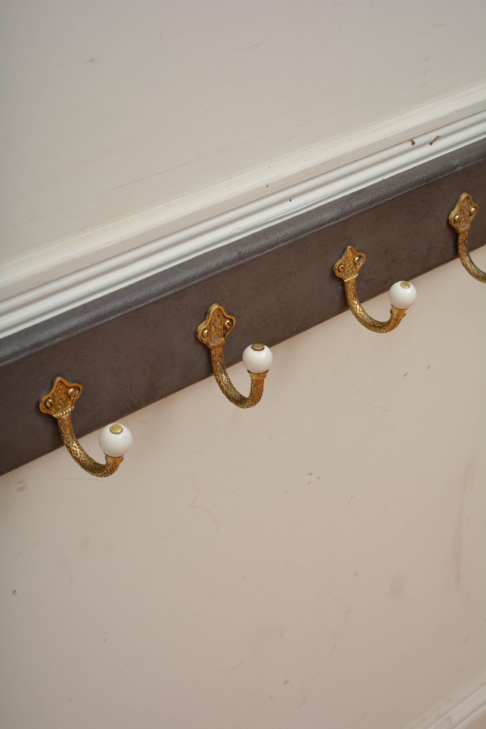A long dark timber wall-mounted coat rack featuring multiple cast brass hooks with white ceramic finials. View III