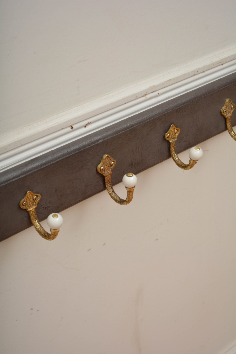 A long dark timber wall-mounted coat rack featuring multiple cast brass hooks with white ceramic finials. View IV
